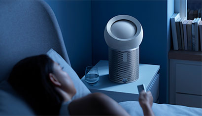 一位女士正在床上使用無線遙控來設定個人空氣淨化風扇的睡眠定時器