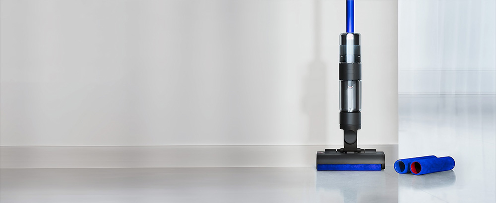 Dyson WashG1立在乾淨的硬質地板上，旁邊有兩個替換超細纖維滾筒