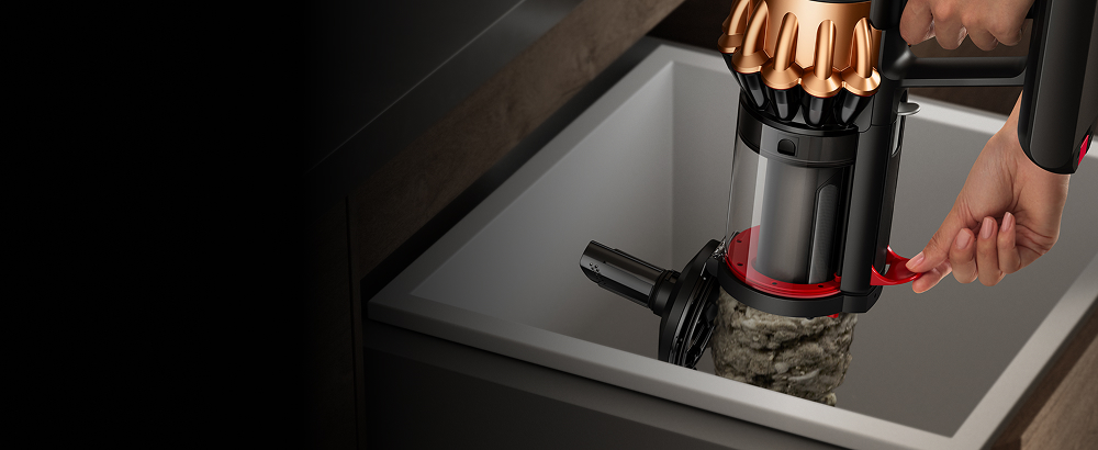 A person wipe-clean emptying the dirt inside the bin of the Dyson Piston Animal vacuum - using the lever on its side.