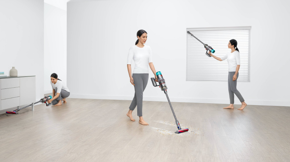 Woman vacuuming a floor, window recess and under furniture in a living area.