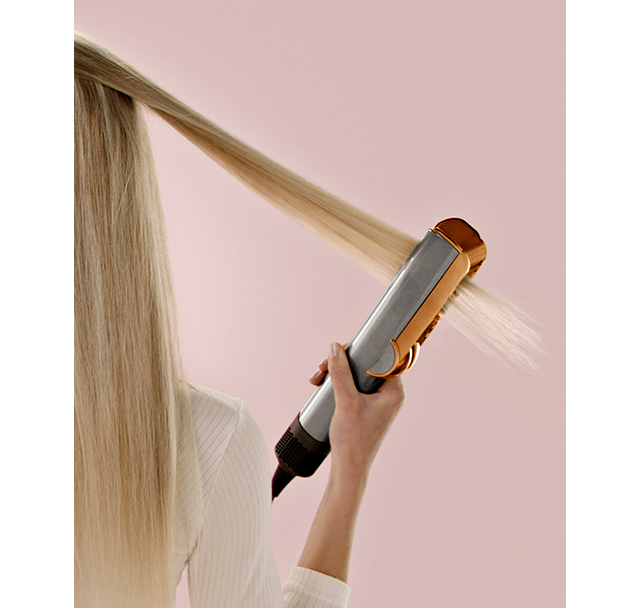 A model uses a Dyson Airstrait on a tress of hair.