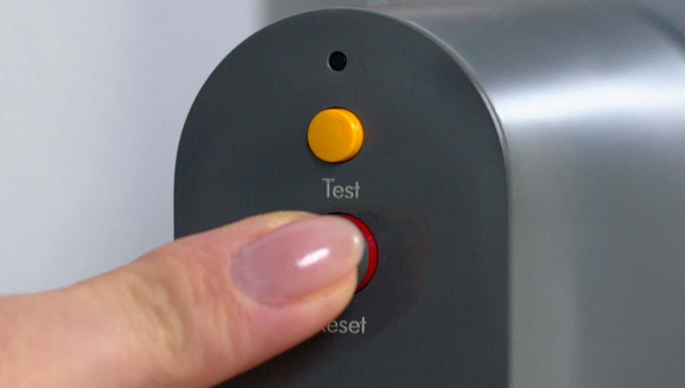 A finger pressing the reset button on the PRCD plug