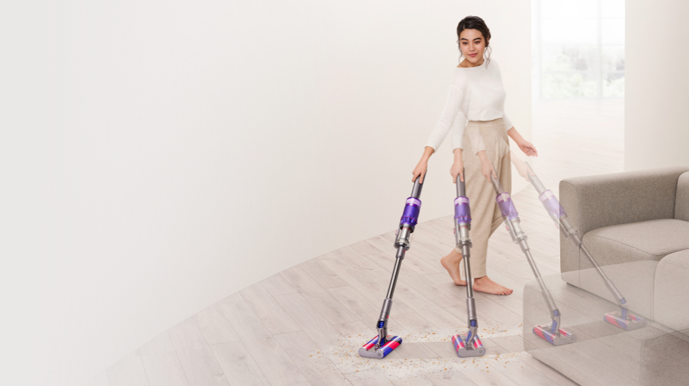 Woman vacuuming hard floor around sofa with the Dyson Omni-glide™ vacuum.